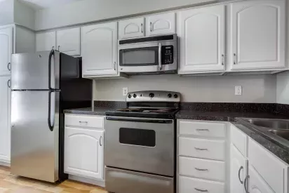 A modern kitchen featuring stainless steel appliances, white cabinets, and dark granite countertops.