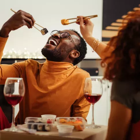 A joyful couple enjoying a cozy evening, sharing sushi and wine in the comfort of their stylish home. The warm ambiance and intimate setting highlight the convenience and luxury of living in an apartment with top-notch amenities perfect for creating memorable moments.