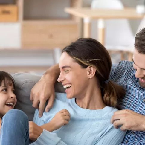 Happy family sitting together on a cozy couch, sharing smiles and laughter, creating a warm and joyful atmosphere in a comfortable home setting.