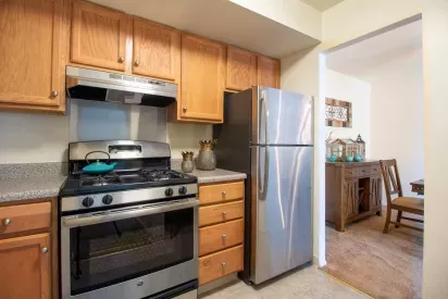 A modern kitchen featuring wooden cabinets, a stainless steel refrigerator, and a polished stove adjacent to a cozy dining space.