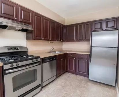  A modern kitchen featuring rich dark wood cabinetry, stainless steel appliances, a gas stove, and a dishwasher, complemented by light countertops and tile flooring.