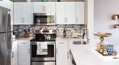 A modern kitchen with stainless steel appliances, white cabinetry, a mosaic tile backsplash, and a sleek countertop featuring decorative accents and a gold centerpiece.