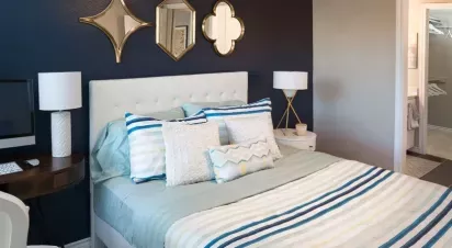 A stylish bedroom with a navy accent wall, decorative mirrors, a tufted white headboard, striped bedding, and modern side tables with lamps.