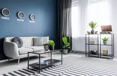 A modern living room with a sleek sofa, striped rug, and clocks displaying different time zones on the wall.