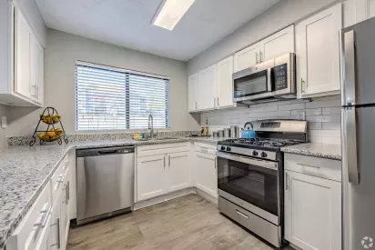 A modern kitchen with white cabinets, granite countertops, stainless steel appliances, and a large window providing natural light.