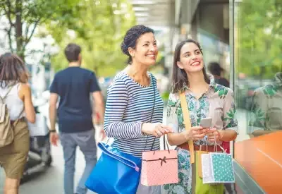 Two women holding shopping bags smiling through a store window