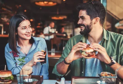 A couple enjoying a casual meal together at a restaurant, smiling and engaging in conversation over burgers and drinks.