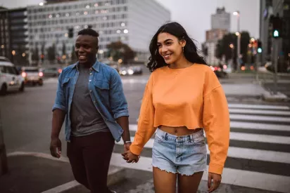 A joyful pair strolling through a bustling cityscape at dusk, with blurred lights and urban buildings in the background, exuding a sense of vibrant energy and connection.