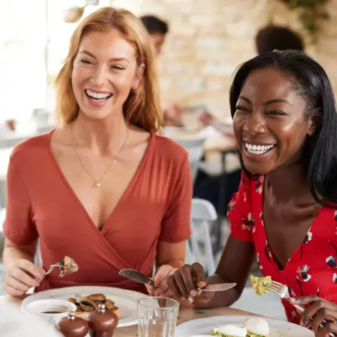 Two women enjoying a meal together, sharing smiles and laughter in a bright, cozy restaurant setting.