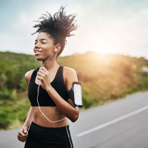 A woman jogging along a winding path while listening to music with the sun shining brightly in the background.