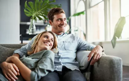 A happy couple relaxes on a comfortable sofa in a bright and stylish living room, surrounded by greenery and natural light.