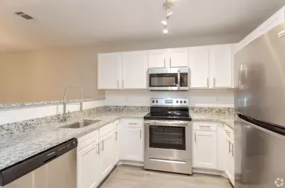 A sleek kitchen with stainless steel appliances, granite countertops, and bright white cabinetry.