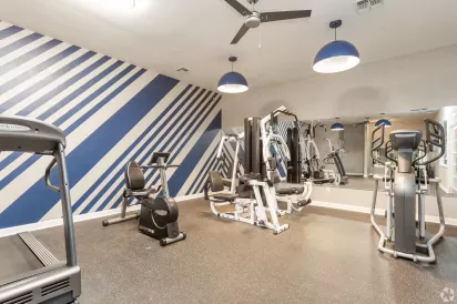 A state-of-the-art fitness center with modern equipment, vibrant wall design, and ceiling fans for a comfortable workout experience.
