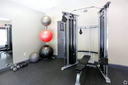 A fully equipped fitness center at Norcross Crossings Apartments featuring modern exercise machines, free weights, and yoga balls, with large windows providing natural light.