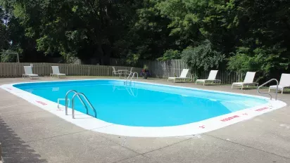 The outdoor pool area at North River Place Apartments, surrounded by lounge chairs, fencing, and trees, offers a refreshing retreat for residents