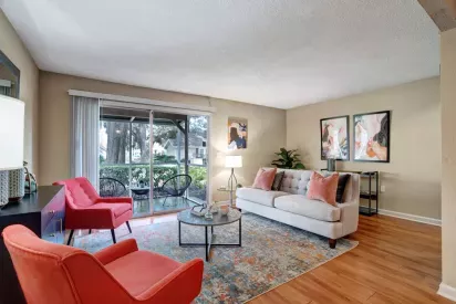 A cozy living room featuring a light gray sofa, red armchairs, and a view of the garden through sliding glass doors.