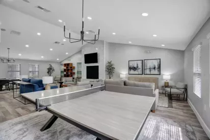 A modern clubhouse interior with a ping pong table, comfortable seating areas, and a fireplace in a bright open space.