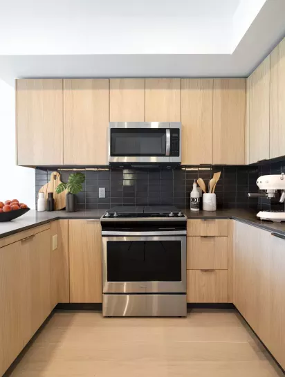 Modern kitchen featuring stainless steel appliances, wood cabinetry, and a sleek tile backsplash at The Edmund Apartments.