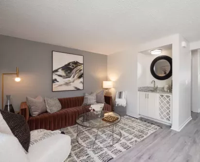 A stylish and modern apartment living room with comfortable seating, a coffee table, and a sleek kitchenette area in the background. The space is beautifully decorated with contemporary artwork and soft lighting.
