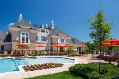 A vibrant outdoor pool area at The Grove Somerset Apartments, featuring cozy lounge chairs, bright orange umbrellas, and a beautifully landscaped backdrop.
