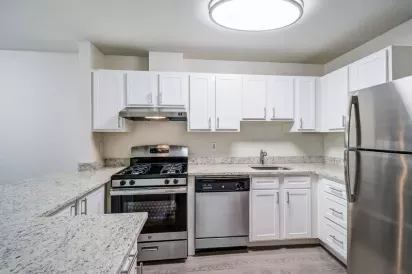 A modern kitchen with white cabinetry, stainless steel appliances, granite countertops, and a sleek overhead light fixture.