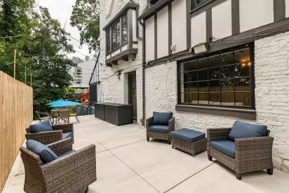 An outdoor patio area featuring cozy wicker chairs with blue cushions, a table with an umbrella, and a charming Tudor-style building in the background.