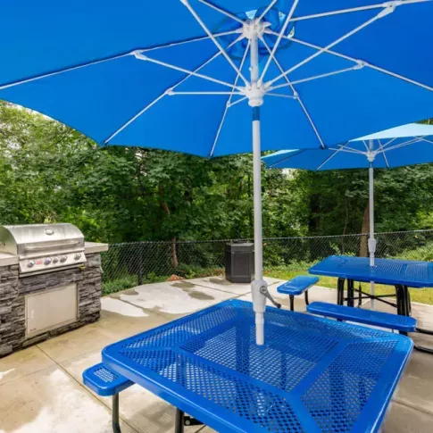 A patio area with blue umbrella-shaded tables and a built-in grill.