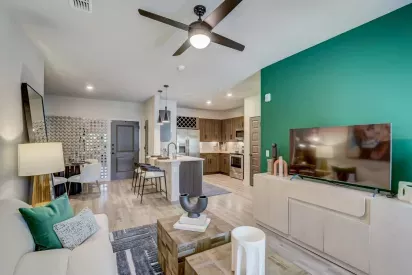 A modern open-concept living room and kitchen with green accent walls, contemporary furniture, and stainless steel appliances at Tropia Wellen Park Apartments.