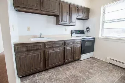 Kitchen area at Washington Gardens Apartments in Washington, NJ, featuring dark wood cabinetry, a single sink, a stove, and a large window allowing natural light.