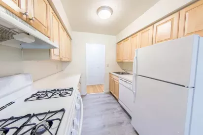 Bright and functional kitchen at The Manors Apartments featuring light wood cabinets, white appliances, and updated flooring, providing a cozy and efficient cooking space.