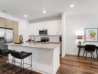 A modern kitchen with stainless steel appliances, white cabinetry, and a granite countertop with barstools.