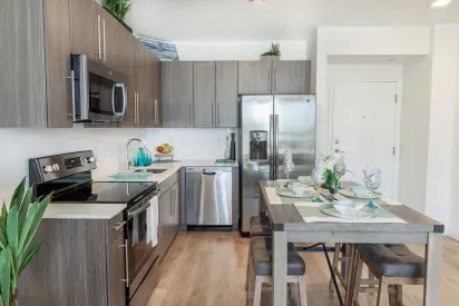 Modern kitchen at 275 Fontaine Parc Luxury Apartments featuring stainless steel appliances, sleek wood cabinetry, and a stylish dining area with elegant place settings.