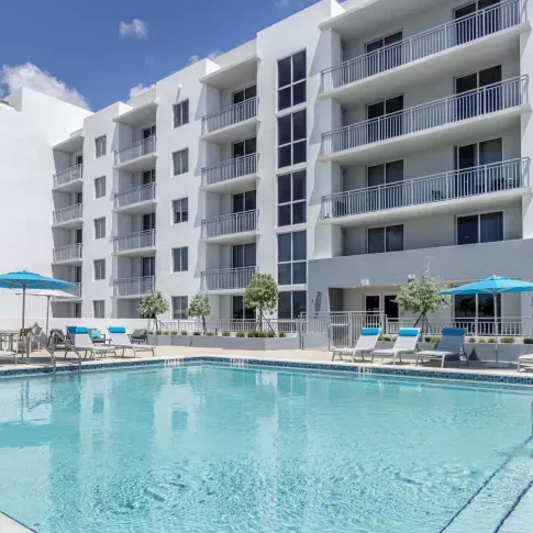 Resort-style pool area at 275 Fontaine Parc Luxury Apartments with sparkling blue water, sun loungers, and contemporary white building facade in the background.