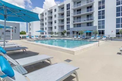 Resort-style pool area at 275 Fontaine Parc Luxury Apartments featuring comfortable lounge chairs, vibrant blue umbrellas, and modern apartment balconies in the background.