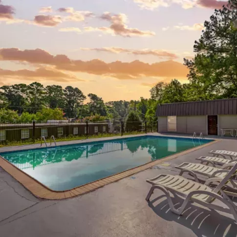 Outdoor swimming pool surrounded by lounge chairs, set against a stunning sunset and lush greenery, offering a peaceful and relaxing atmosphere for residents.