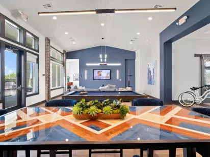 A bright community lounge with a colorful geometric dining table and a pool table in the background.
