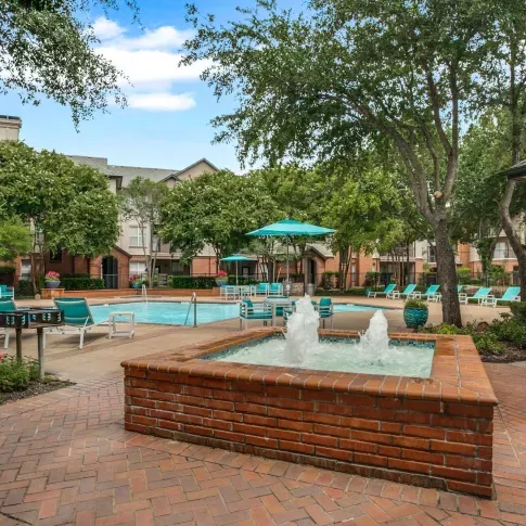 A serene courtyard with a bubbling fountain, landscaped pathways, and views of the swimming pool.