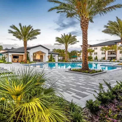 A tranquil poolside setting with lounge seating and a clubhouse, surrounded by vibrant greenery and palm trees.