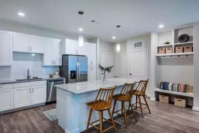 A modern kitchen featuring white cabinetry, stainless steel appliances, granite countertops, and pendant lighting over a spacious island with wooden barstools.