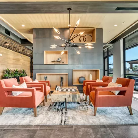 A vibrant social space with bold orange armchairs arranged around a chessboard, complete with a modern light fixture and artistic shelving.