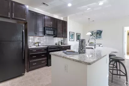 A sleek kitchen featuring dark wood cabinets, a granite countertop, and a breakfast bar with stools under pendant lights.