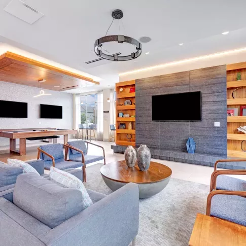 A sophisticated resident lounge featuring plush seating, a billiards table, mounted flat-screen TVs, and sleek modern décor, designed for comfort and socializing.
