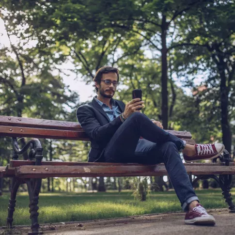 Man sitting on park bench while looking at phone