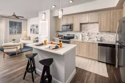 A contemporary open-concept kitchen with light wood cabinets, stainless steel appliances, and a chic breakfast bar connecting to the living area.