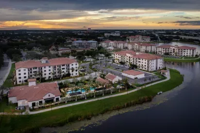 A stunning aerial shot of Locklyn West Palm Luxury Apartments at dusk, showcasing Mediterranean-style buildings, lush landscaping, and a resort-style pool by the lake.