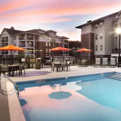 A stunning sunset over the pool area, reflecting soft colors in the water, with orange umbrellas and lounge chairs for relaxation.