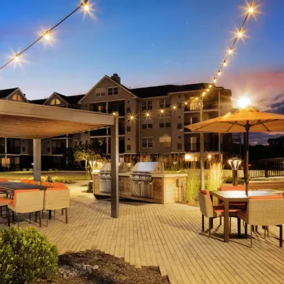 A well-lit communal outdoor space with modern grilling stations, a covered dining area, and ambient string lighting for an inviting evening setting.