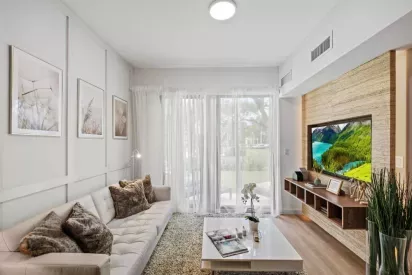 The Oak Enclave apartments offer a modern living space with a mounted TV, floor-to-ceiling windows, and an inviting atmosphere.