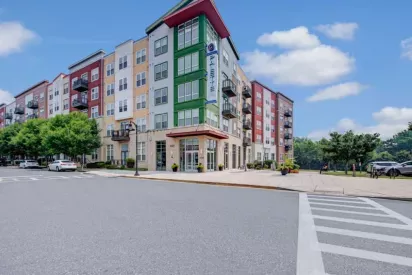 The exterior view of a colorful multi-story apartment building with landscaped sidewalks and a corner entrance.