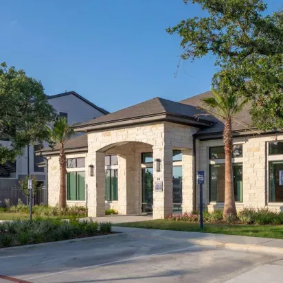 Grand clubhouse exterior with stone-accented architecture, lush landscaping, and a welcoming entrance that sets the tone for luxury living.